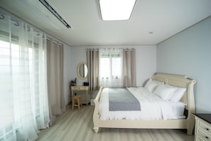 A bedroom with a bed, a nightstand, a dresser, a mirror, and a window with curtains. - rabbit foot renthouse (Jeju City)