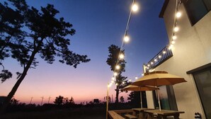 Un patio con luces colgantes, mesas de madera y sombrillas.