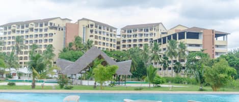 A resort with a swimming pool, lounge chairs, and a thatched-roof hut.