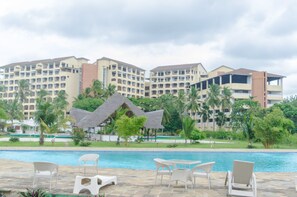 Un resort con piscina, lettini e una capanna dal tetto di paglia.