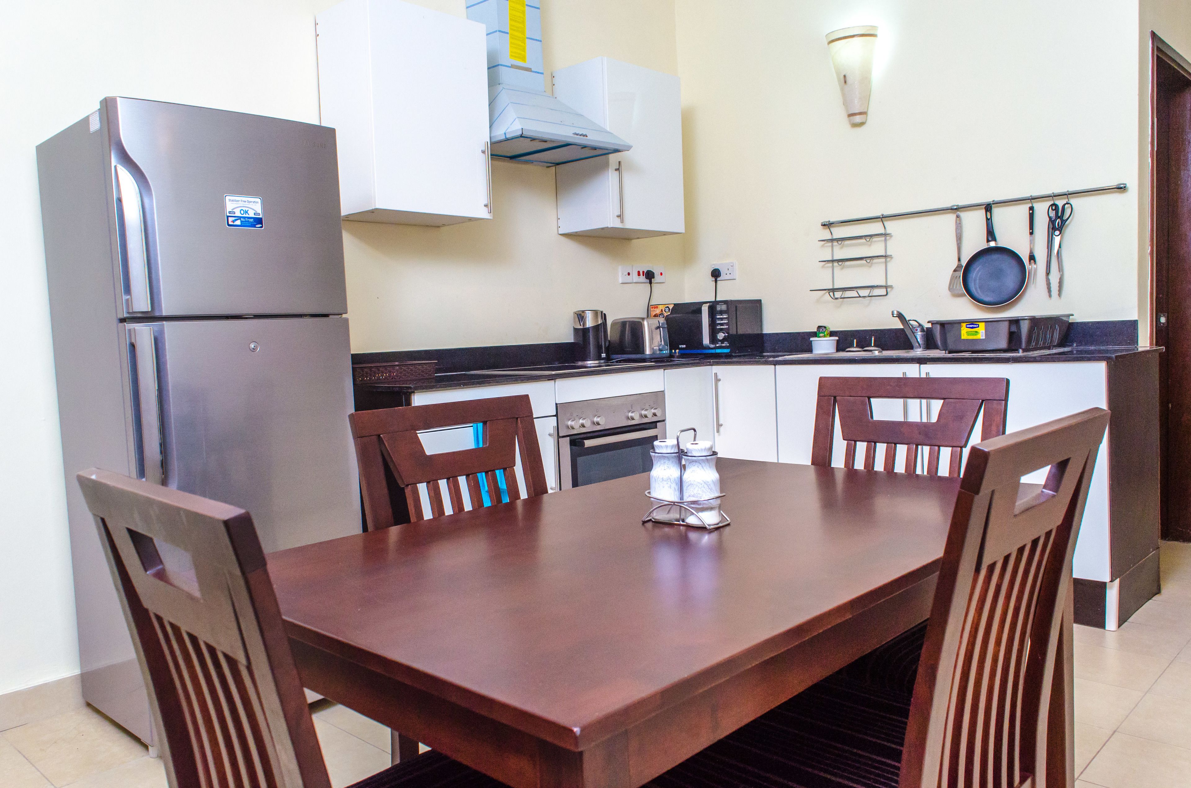 A compact kitchen with a refrigerator, stove, microwave, and a dining table with chairs.