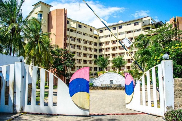 Un edificio a più piani con ingresso recintato, palme e cielo sereno.