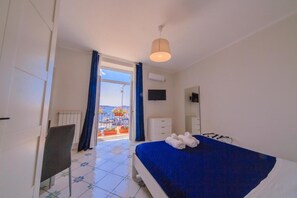 A hotel room with a bed, a chair, a dresser, a mirror, and a view of the sea through a large window. - Casa Adele b&b (Pozzuoli)