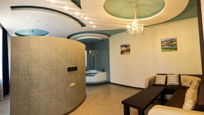 A modern hotel room with a curved ceiling, a chandelier, a sofa set, and a large cylindrical column. - Hotel Lider Complex (Vayk)