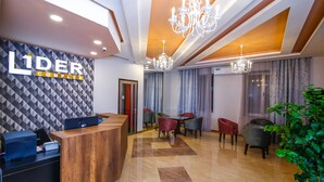 A hotel reception area with a wooden reception desk, a patterned wall, and a chandelier. - Hotel Lider Complex (Vayk)