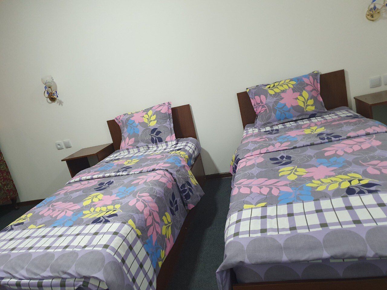 Two single beds with floral-patterned bedding, wooden headboards, and nightstands with lamps.