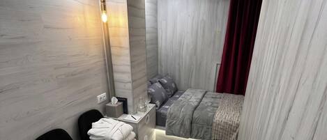 A compact bedroom with a bed, bedside table, chair, and a small desk area.