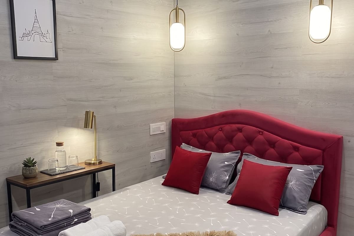 Ein modernes Schlafzimmer mit einem roten, gepolsterten Kopfteil, einem Nachttisch mit Lampe und einem gerahmten Bild an der Wand.