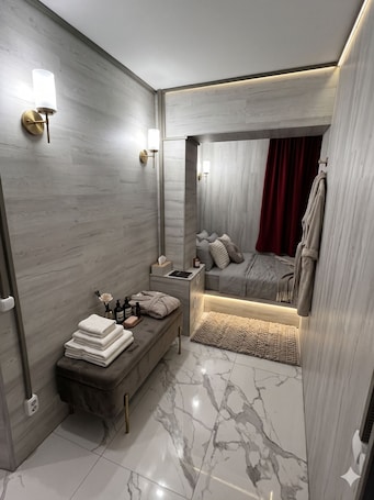 A modern bathroom with a marble floor, a vanity with a towel stack, a bench, and a shower area with a red curtain.
