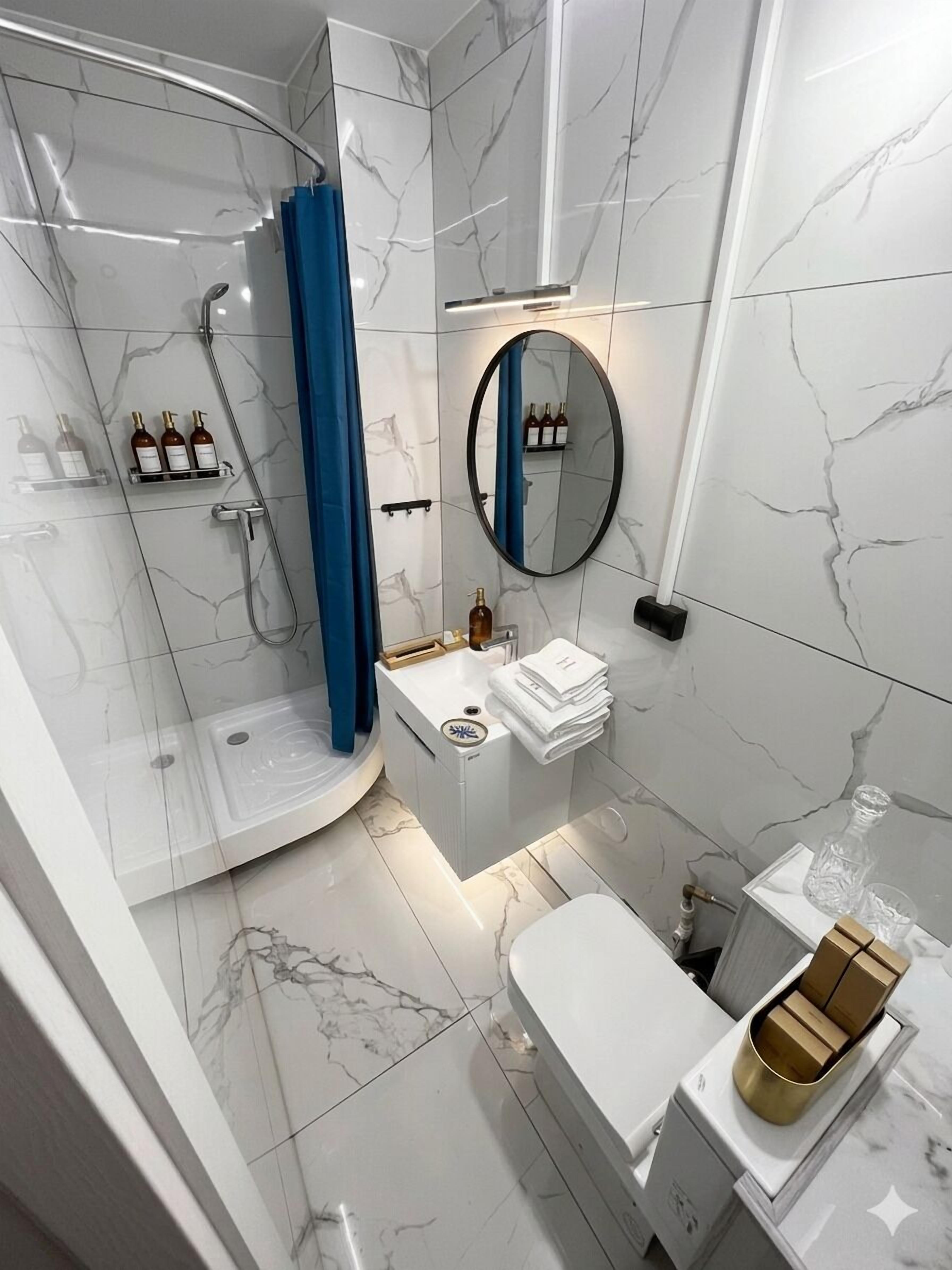 Une salle de bain moderne avec une douche à forme incurvée, un miroir rond, des toilettes et un lavabo.