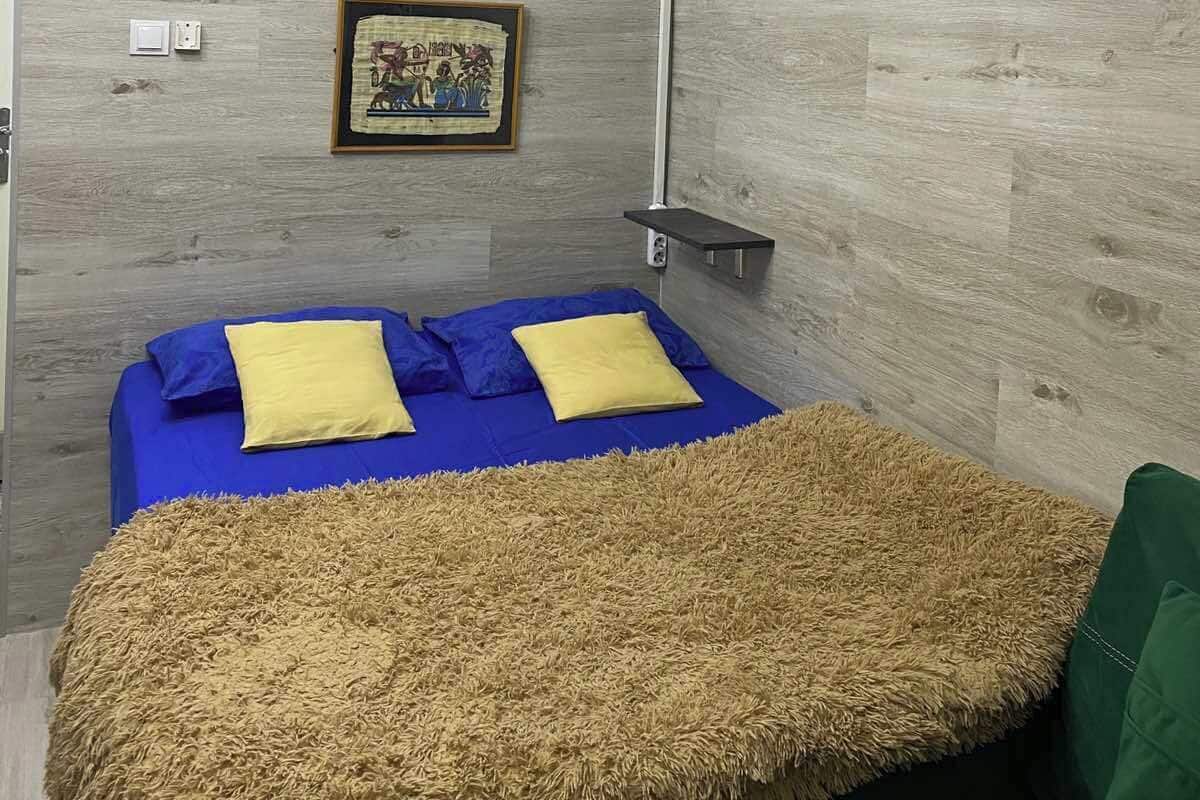 Ein Zimmer mit einem Bett, einem gerahmten Bild an der Wand und einer Deckenleuchte.