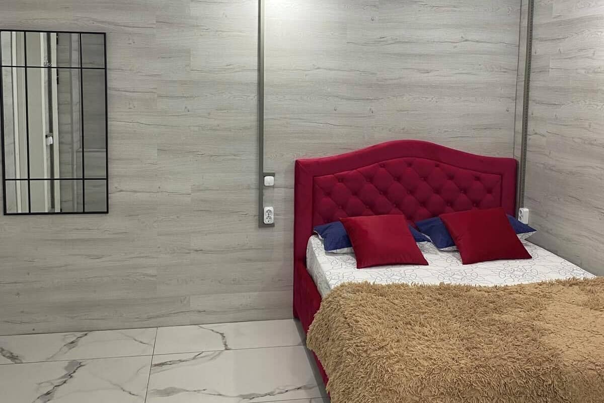 Ein Schlafzimmer mit einem Bett, einem Fenster mit Jalousien, einer Leuchte und einer Steckdose.