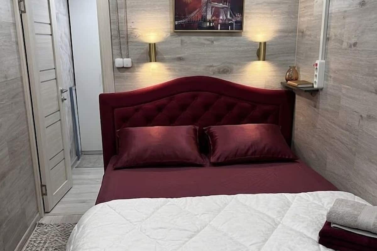 Ein Schlafzimmer mit einem roten, gepolsterten Kopfteil, einer weißen, gesteppten Bettdecke und einem gerahmten Bild über dem Bett.
