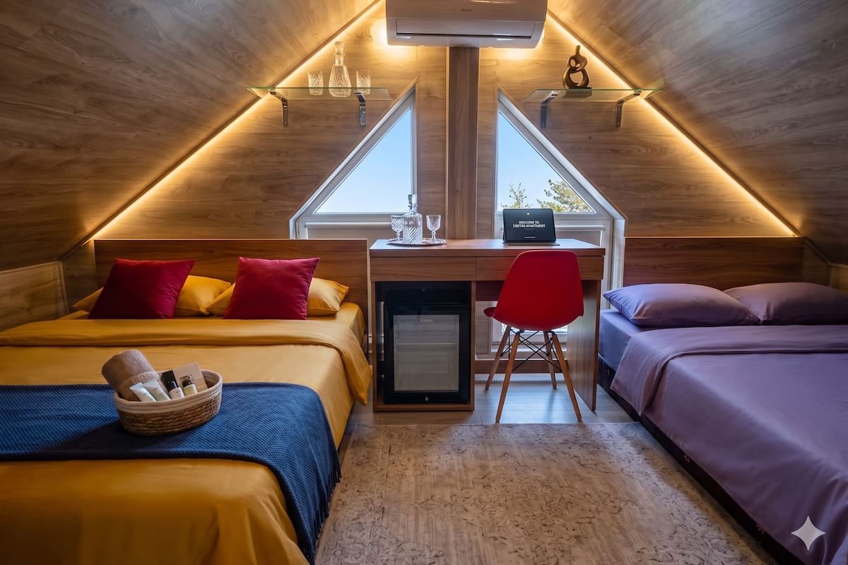 Ein gemütliches Schlafzimmer im Dachgeschoss mit schrägen Wänden, einem Schreibtisch mit einem Laptop und zwei Betten mit farbenfroher Bettwäsche.