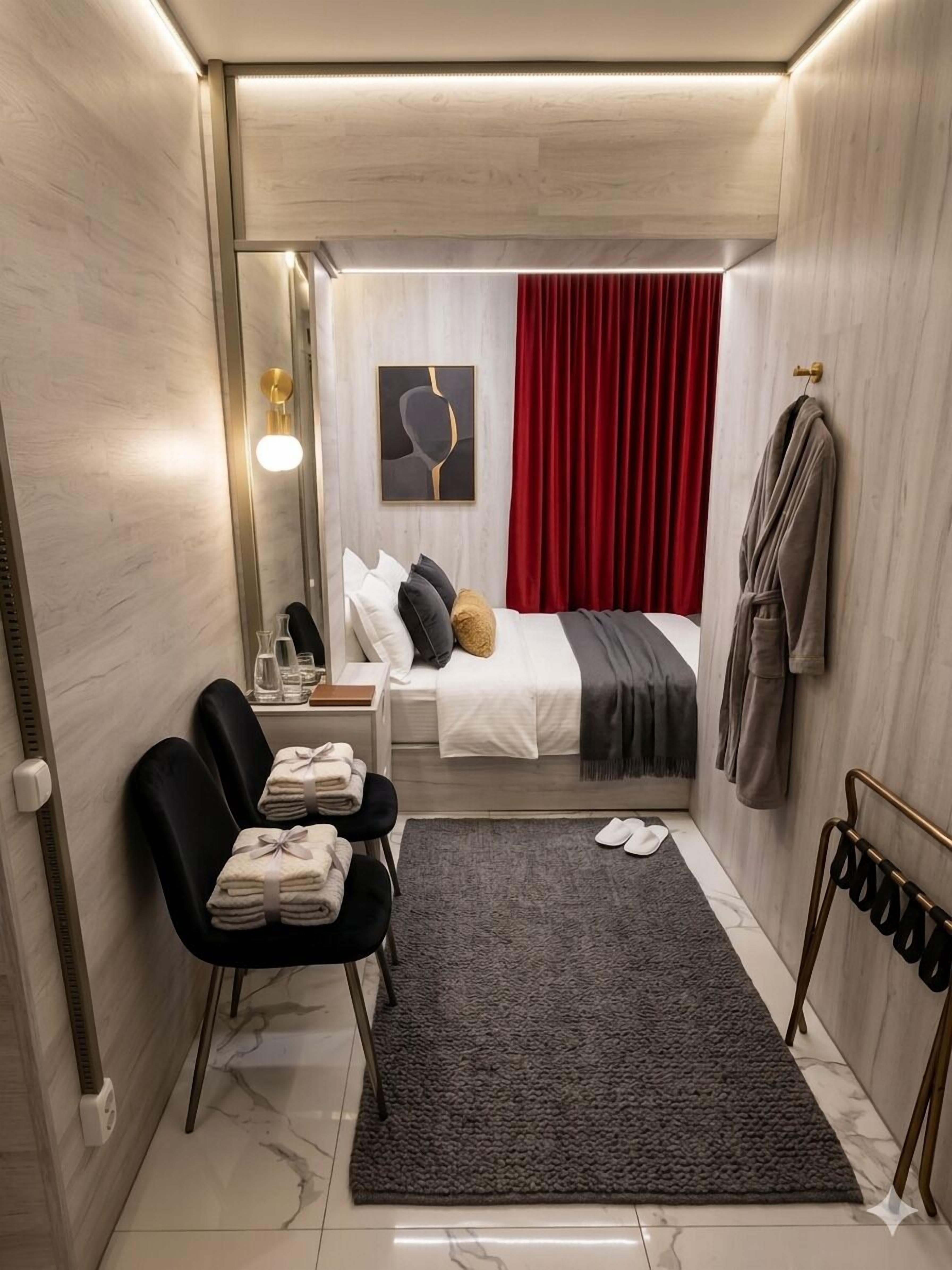 Ein kleines Hotelzimmer mit einem Bett, einem Schreibtisch, einem Stuhl, einem Bademantelständer und einem Teppich.