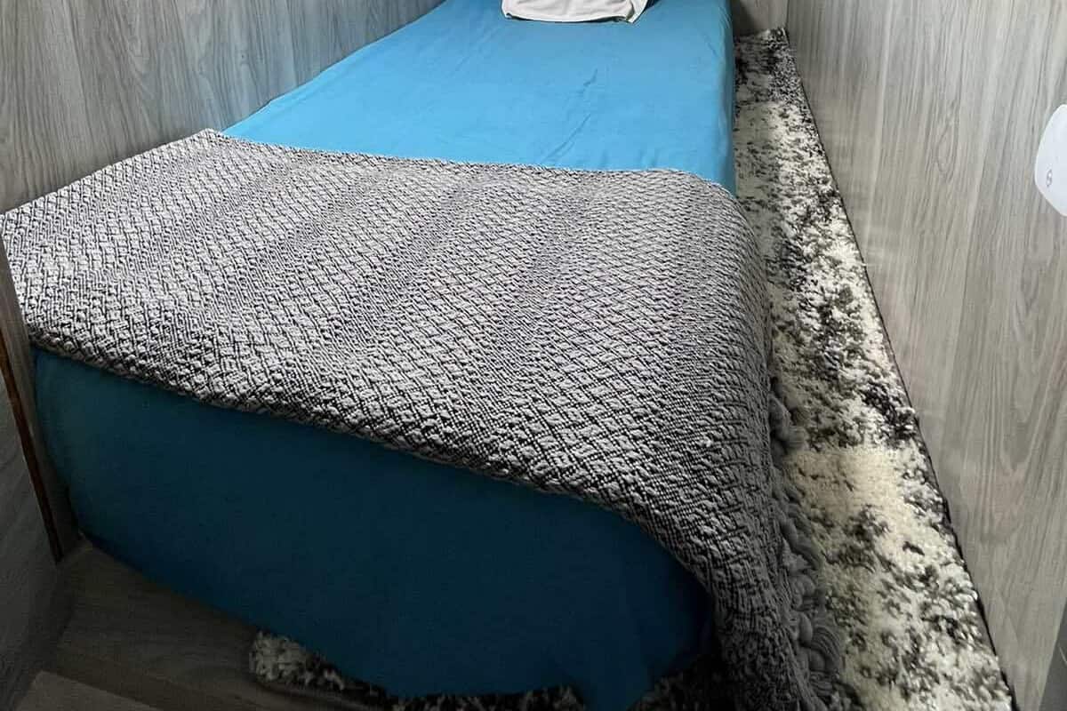 Ein kleines, kompaktes Zimmer mit zwei Betten, einem Wandheizkörper und einem Deckenventilator.