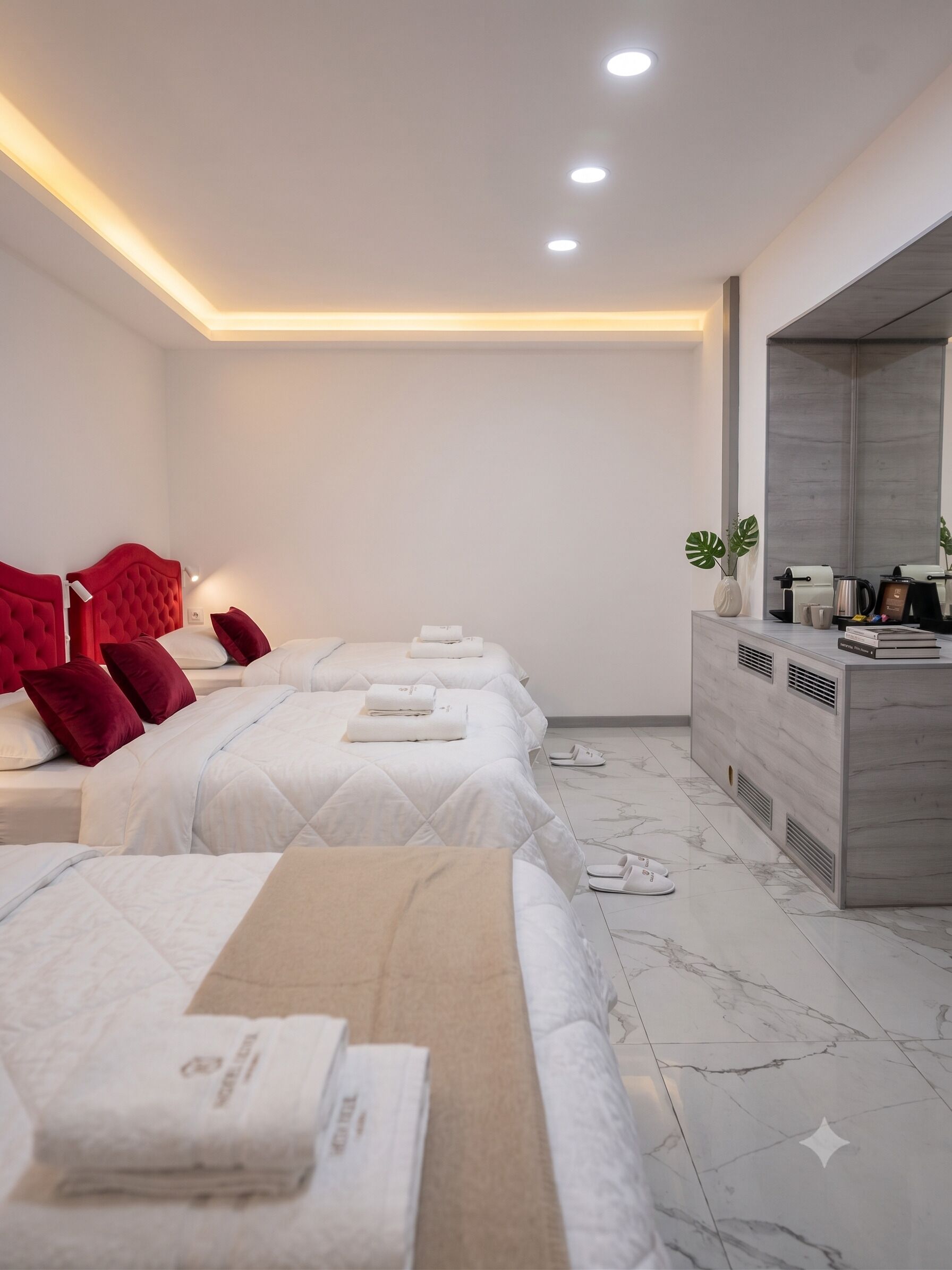 A hotel room with three beds, a vanity with a mirror, and a marble floor.