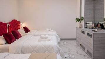 A hotel room with three beds, a vanity with a mirror, and a marble floor.