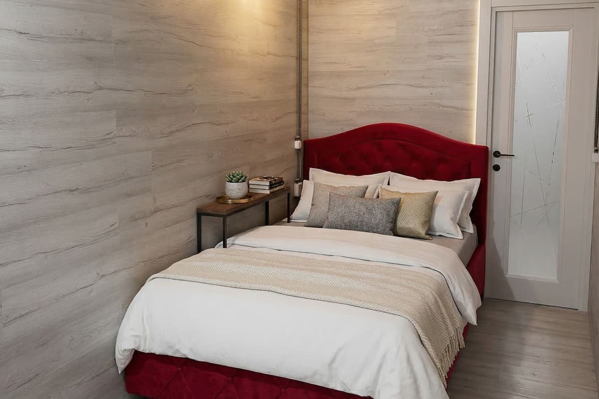 Ein Schlafzimmer mit einer Holzwand, einem roten, mit Stoff bezogenen Kopfteil, einem Nachttisch mit Lampe und einer Tür.