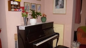 Ein Zimmer mit Klavier, Gitarre, einer kleinen Hocker und einem Regal mit Büchern und Dekoration.