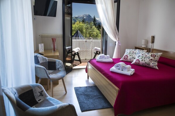 Een slaapkamer met een houten bed, een rode sprei en uitzicht op bergen door een geopende deur.
