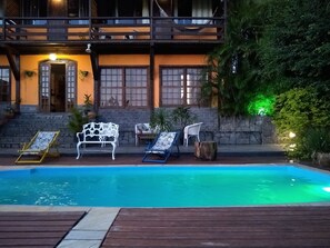 A pool area with lounge chairs and a stone wall. - Mira Playa Geribá (Búzios)