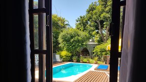 An open door revealing a wooden deck with a pool, surrounded by lush greenery and a stone structure. - Mira Playa Geribá (Búzios)