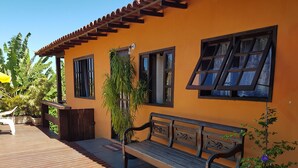 A wooden deck with a bench, a potted plant, and a building with a tiled roof and windows. - Mira Playa Geribá (Búzios)