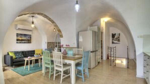 Een ruime woonkamer met een eettafel, stoelen en een bank. Er is een keuken aanwezig met een koelkast en een trap die leidt naar een ander niveau.
