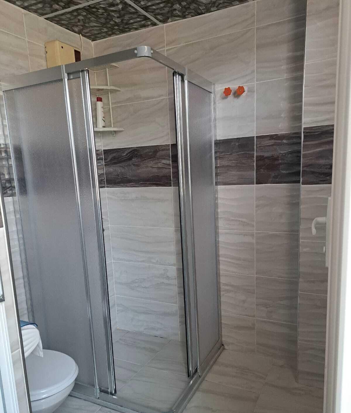 A bathroom with a glass-enclosed shower, tiled walls, and a toilet.