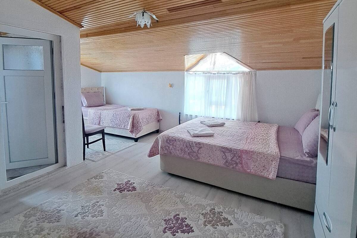 Ein Schlafzimmer mit zwei Betten, Holzboden, einem großen Fenster mit Vorhängen und einem gemusterten Teppich.