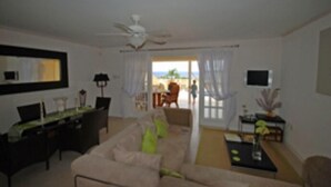 A living room with a sofa, a coffee table, a TV, and a ceiling fan. There is a view of the outside through a glass door. - 2 Westlook (Gibbes)