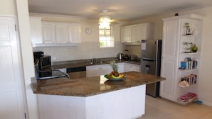 A kitchen with white cabinets, a granite countertop, a stainless steel refrigerator, and a fruit bowl on the island. - 2 Westlook (Gibbes)
