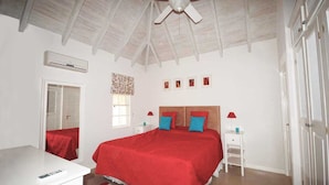 A bedroom with a large bed, a ceiling fan, a window with a curtain, and a white bedside table with a lamp. - 2 Westlook (Gibbes)