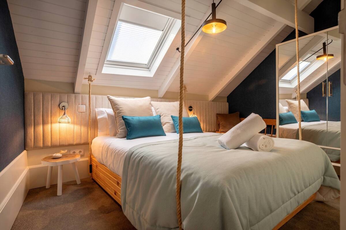 A bedroom with a large bed, a small bedside table, a mirror, and a skylight.