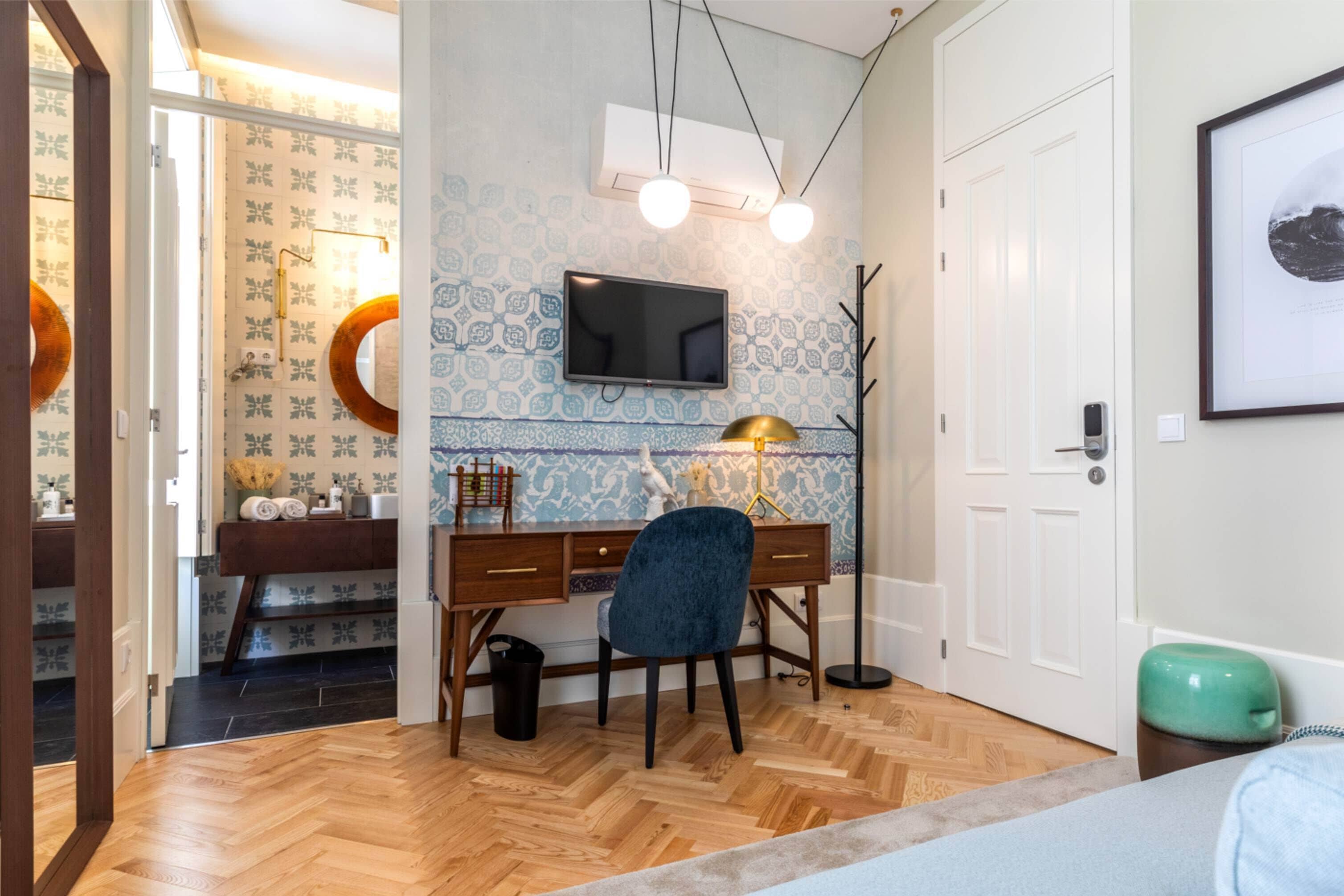 A room with a wooden herringbone floor, a desk with a chair, a flat-screen TV, and a framed picture on the wall.