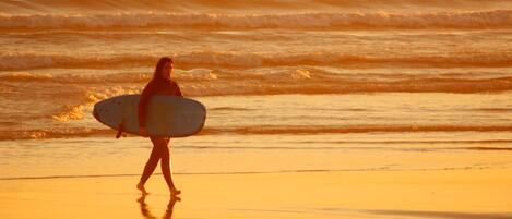 A person carrying a surfboard on a beach during sunset.