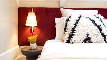 A neatly made bed with white and black patterned pillows, a red headboard, and a bedside table with a lamp and a vase of flowers.