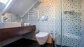 Un baño moderno con tragaluz, inodoro blanco, cabina de ducha de vidrio y salpicadero con diseño.