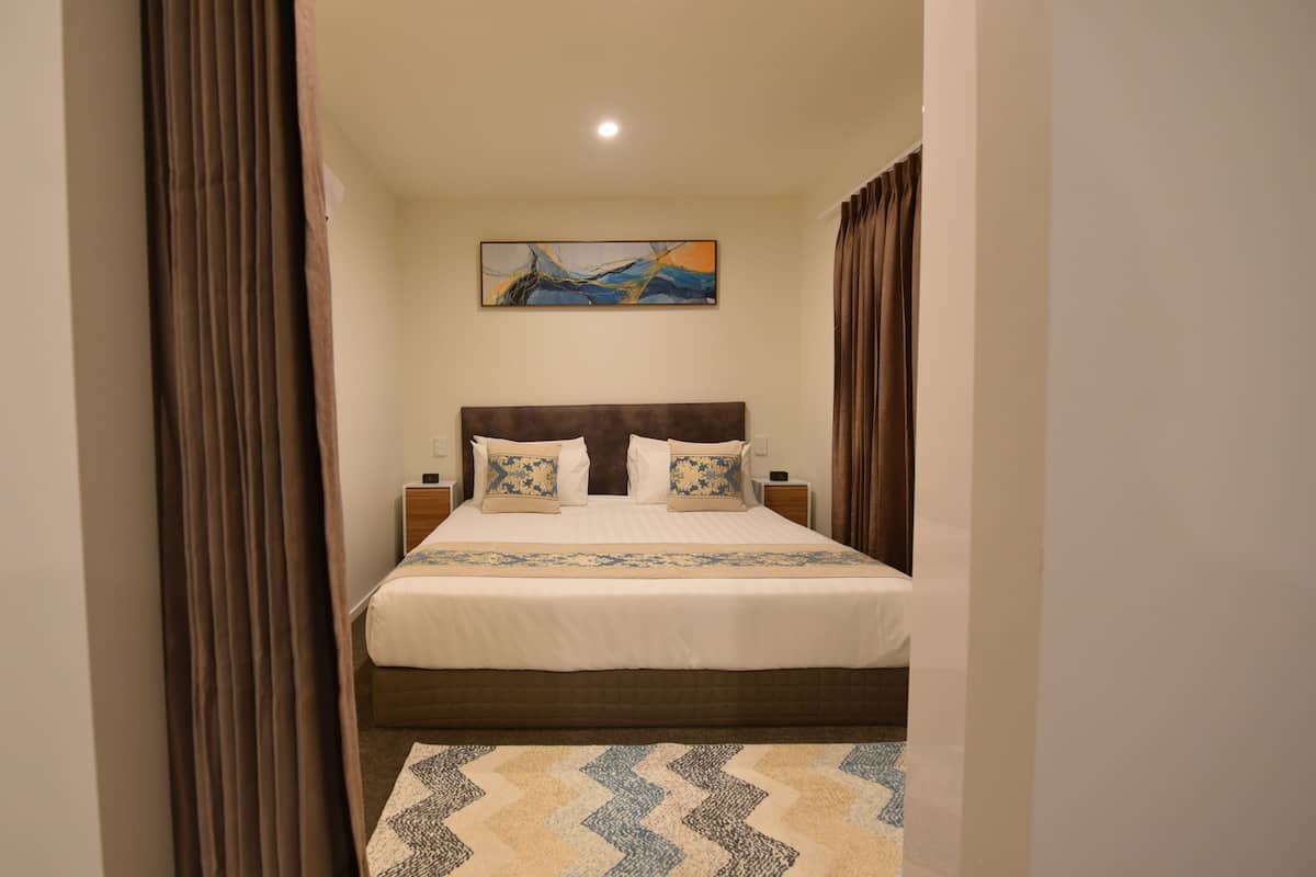 Quarto de hotel com cama, mesa de cabeceira, abajur e um quadro na parede.