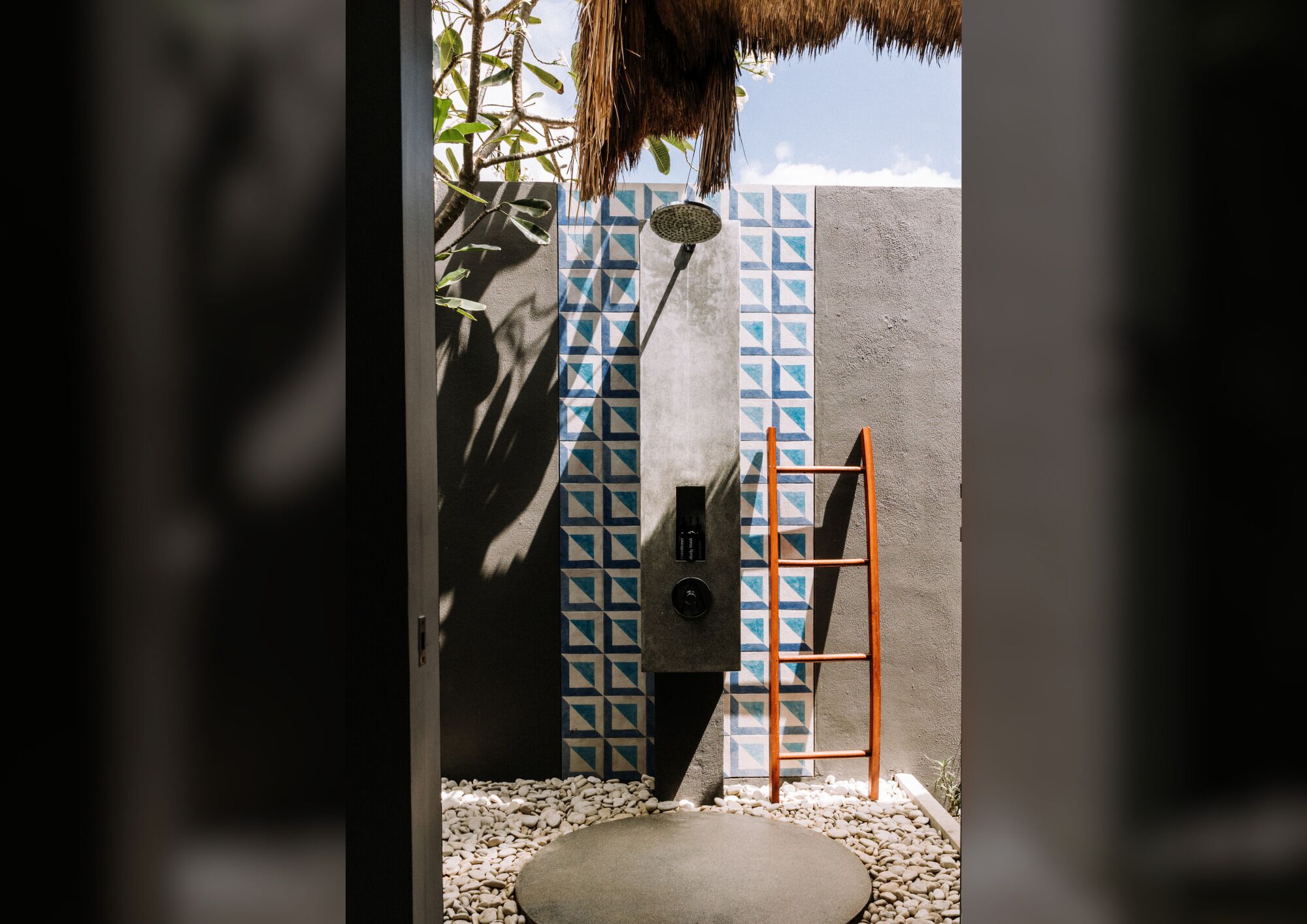 A modern bathroom with a geometric tile pattern, a shower, and a wooden ladder.