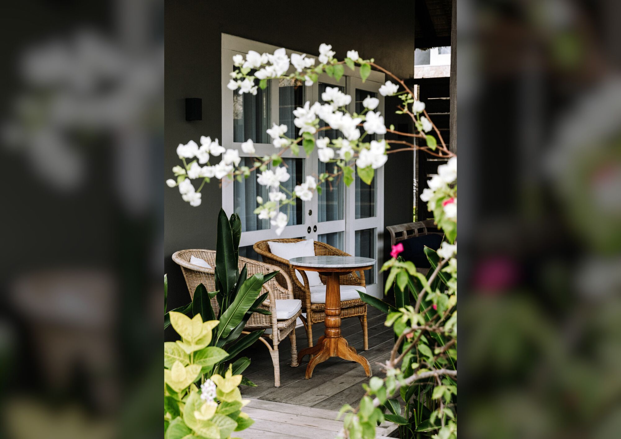 Un patio con muebles de mimbre, una mesa redonda y flores blancas.