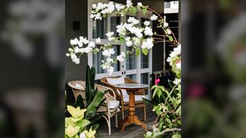 Un patio con muebles de mimbre, una mesa redonda y flores blancas.