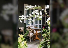 Un patio con muebles de mimbre, una mesa redonda y flores blancas.