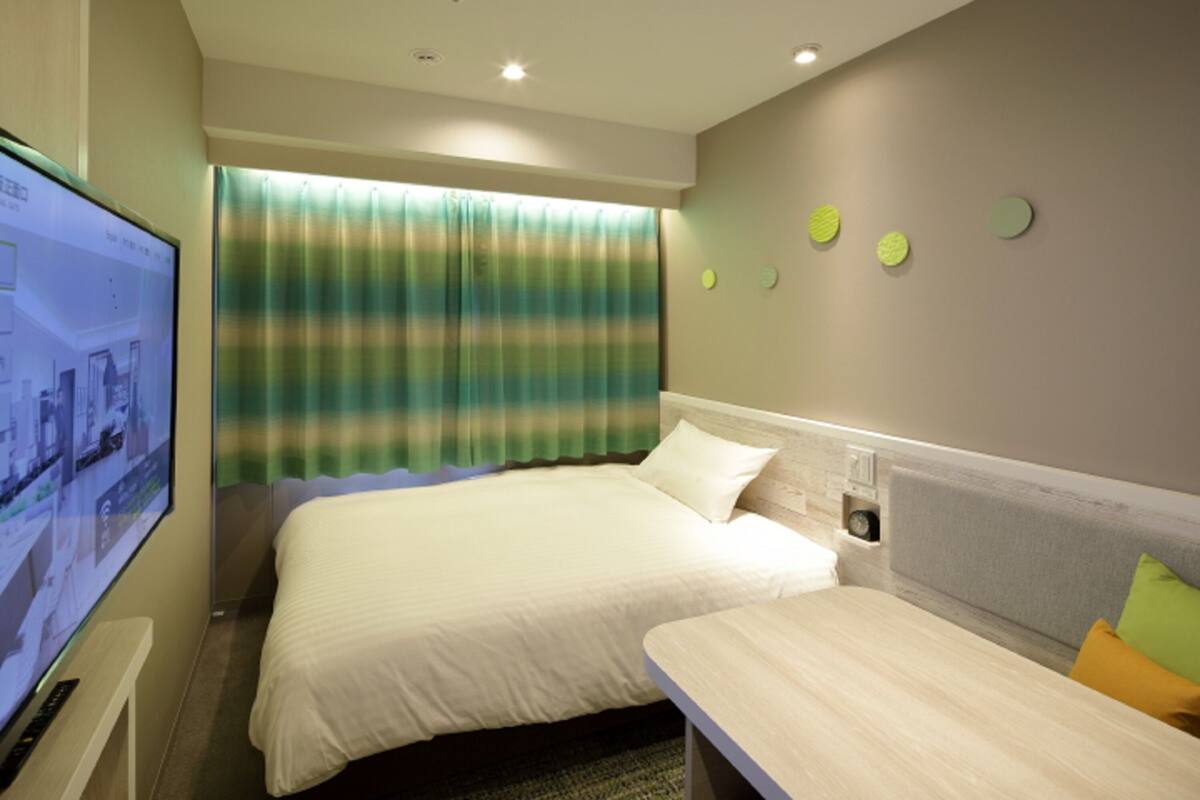 A hotel room with a bed, a desk, a television, and a window with curtains.