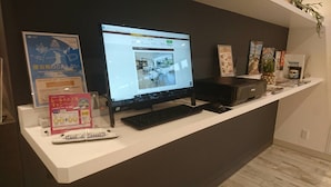 Een receptiebalie met een computer waarop een webpagina, toetsenbord, muis en printer worden weergegeven. Op de balie staan posters en een klein modeltreintje.