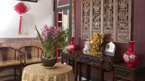 A traditional room with a round table, chairs, a red vase, a golden statue, and intricate wooden panels. - Shuitou Inn I (Jincheng)