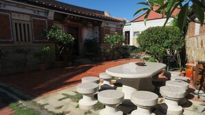 A courtyard with a stone table and stools, surrounded by potted plants and a traditional building with a tiled roof. - Shuitou Inn I (Jincheng)