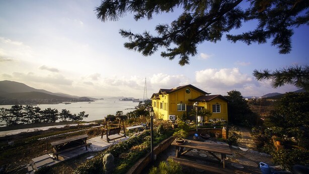 A yellow house with a view of a body of water and mountains in the background. - Tongyeong MongDol House (Tongyeong)