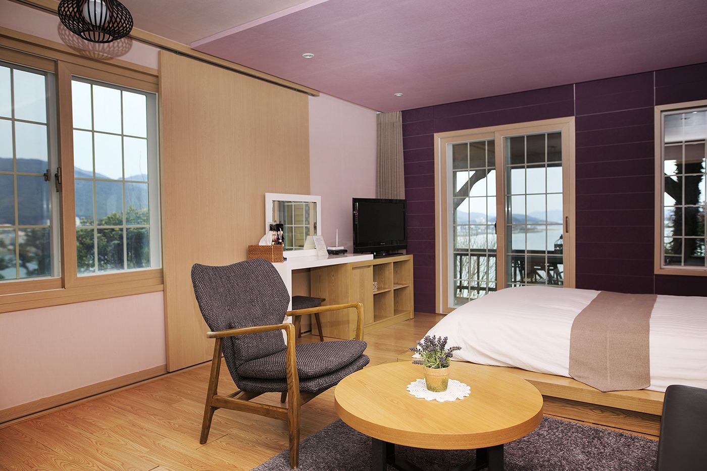 Ein Hotelzimmer mit Bett, Schreibtisch mit Fernseher, Stuhl, kleinem Tisch und großen Fenstern mit Blick.